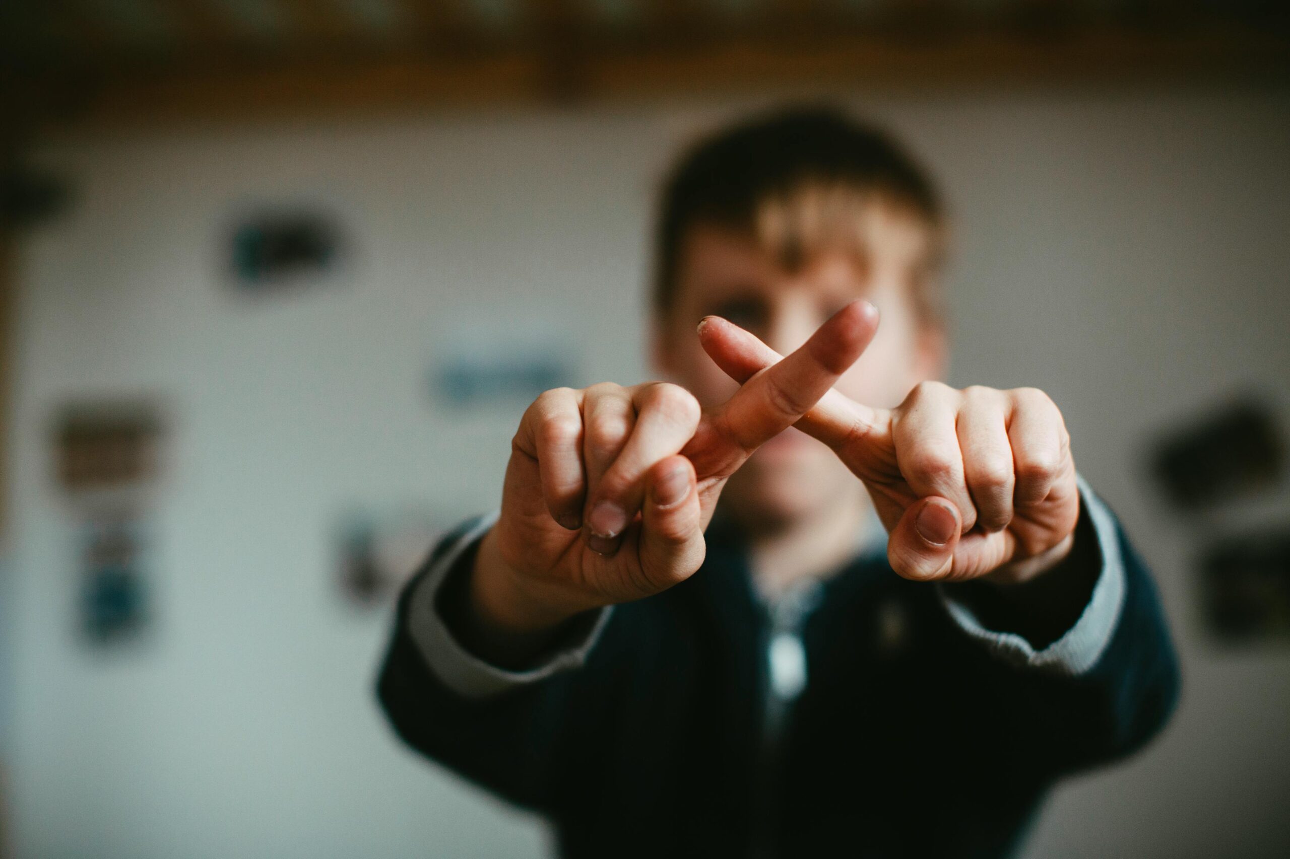 Close-up of a child crossing fingers in an indoor setting with a blurred background.